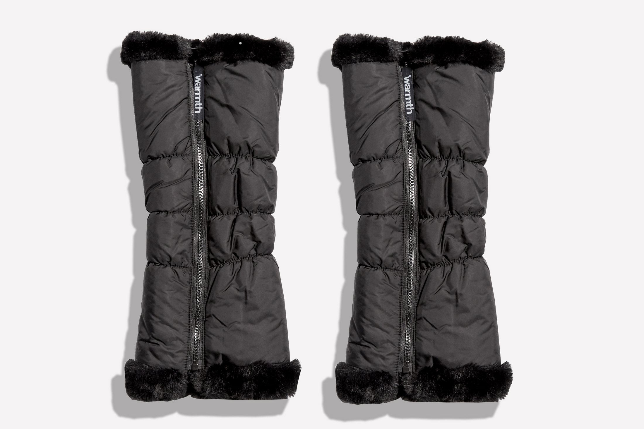 Pair of black puffer leg warmers with zipper pulls with fur trim on a white background
